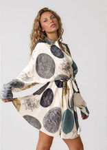Woman wearing a flared mini dress with long sleeves and a self-tie waist belt in a unique designer pattern